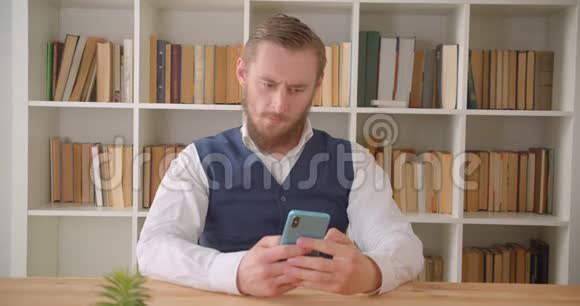 一位年轻的白种人商人用手机在办公室里看着摄像机的特写照片视频的预览图