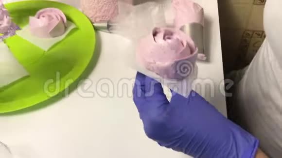 一个女人把一朵棉花糖玫瑰放在托盘上桌子上有一个容器里面有棉花糖和其他制作棉花糖的工具视频的预览图