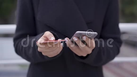 一个穿着黑色外套的年轻女人用手机和信用卡在网上付款支付方便现代视频的预览图