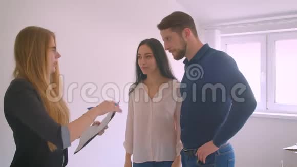 年轻的白种人夫妇签署文件并从他们的新公寓钥匙从房地产经纪人兴奋视频的预览图