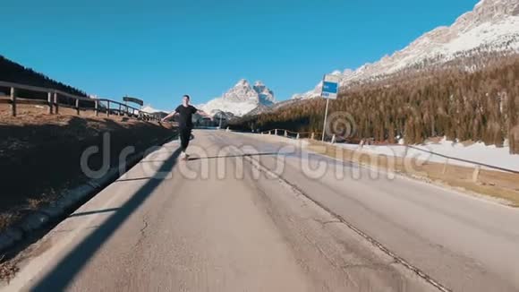 在森林和山脉的背景下年轻人骑着一个小滑板在路上视频的预览图