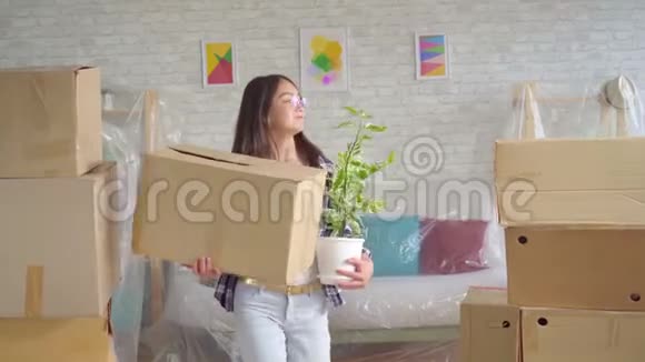 一位手里拿着一朵花和一个盒子的积极的年轻女士搬到了一间新公寓视频的预览图