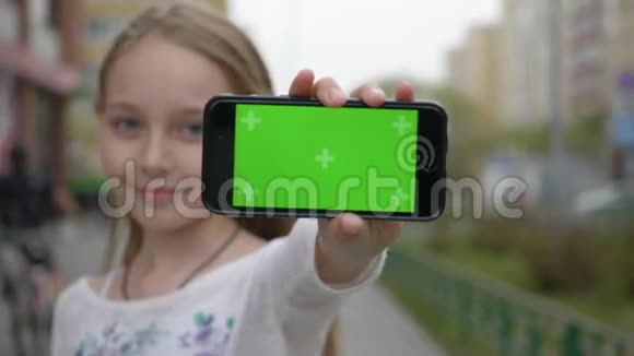 十几岁的女孩在城市街道上用绿色屏幕对着镜头显示手机紧紧地抱着少女视频的预览图
