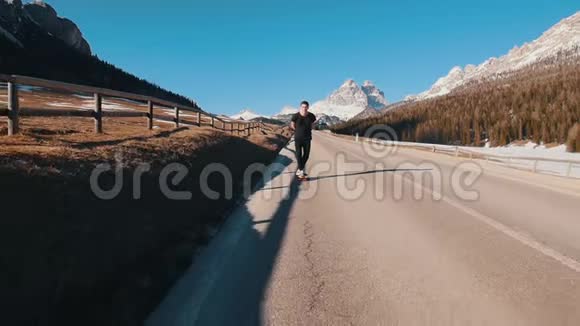 年轻人骑在马路上在阿尔卑斯山中间的一个小滑板里保持平衡视频的预览图