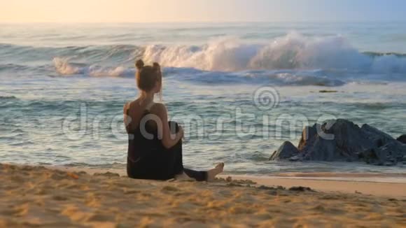 穿黑色衣服的苗条女士乘海浪在沙滩上冥想视频的预览图