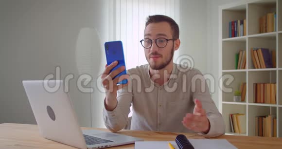 一位年轻英俊的白种人商人的特写肖像他在电话上打了一个视频电话兴高采烈地坐在其中视频的预览图