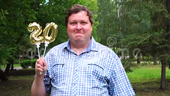大个子拿着金色气球在户外做20个数字20周年庆祝晚会视频的预览图