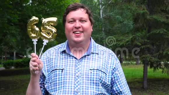 大个子拿着金色气球把65号的号码放在户外65周年庆祝晚会视频的预览图