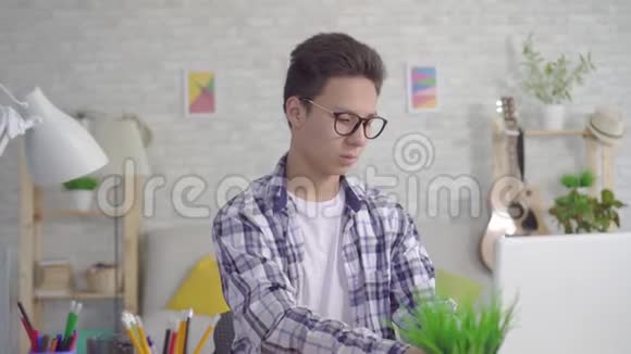 体贴的亚洲年轻人戴着时髦的眼镜在家里的客厅里用笔记本电脑工作视频的预览图