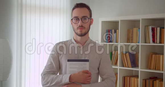 年轻英俊的白种人男学生戴着眼镜举着一本书看着站在镜头里的镜头视频的预览图
