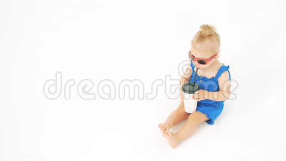 戴墨镜的小女孩在白色背景上用吸管从纸杯里喝饮料视频的预览图