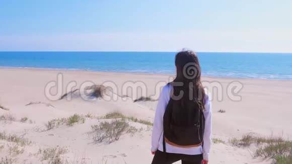 女人站在沙丘间的海边沙滩上眺望海上度假的后景视频的预览图