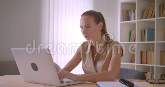 优雅的白种人女商人分析笔记本电脑上的数据转向相机在办公室里愉快地微笑视频的预览图