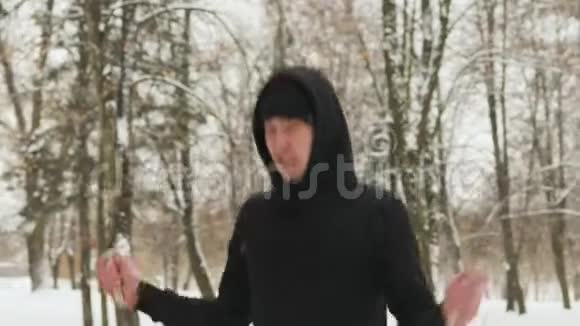 穿着黑色运动服的年轻人在寒冷的天气里在一个白雪覆盖的公园里做运动跳绳来自视频的预览图