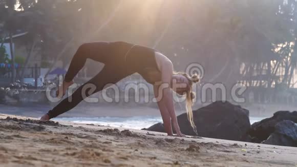 美丽的黑发女人举起手和腿在海滩上做瑜伽视频的预览图