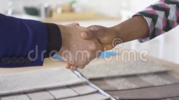 高加索男人和非裔美国妇女的特写镜头在桌上摆着的室内装潢中握手视频的预览图
