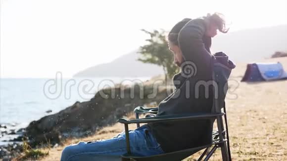 年轻人坐在湖岸露营地的椅子上挽着发髻视频的预览图