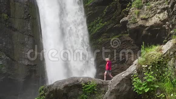 穿着红色夹克衫在大瀑布附近散步的女人视频的预览图