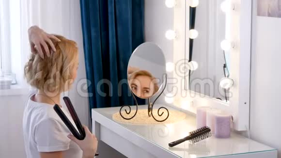 年轻的金发女人把头发卷在钳子上陶瓷矫直机视频的预览图