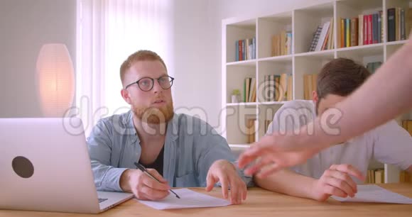两名成年白人员工使用笔记本电脑在办公室进行室内讨论的特写照片视频的预览图