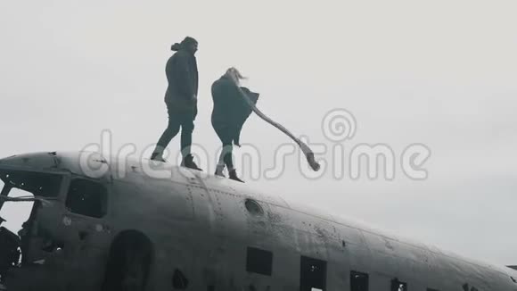 在多风的阴天年轻的旅行夫妇在冰岛坠毁的DC3飞机顶部行走视频的预览图