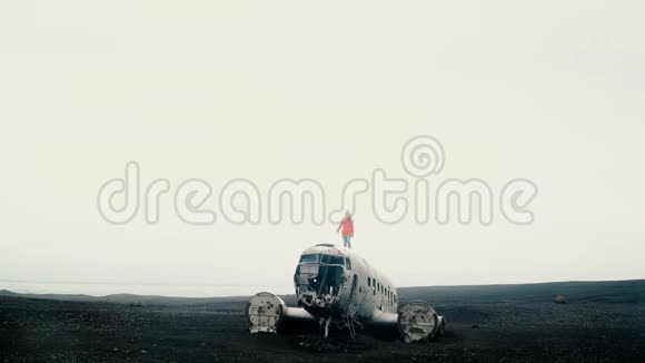 穿着粉红色夹克的年轻女子站在冰岛坠毁的DC3BMC的顶部环顾黑色海滩视频的预览图