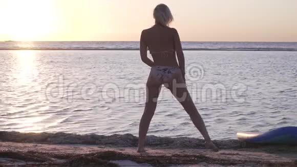 在海滩上锻炼年轻的女人在伸展明亮的日落在地平线上视频的预览图