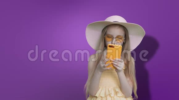 十几岁的女孩戴着夏帽在紫丁香的墙背景上读电话阿尔法频道视频的预览图