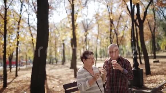 一对年长的夫妇在秋天公园喝咖啡或塑料杯茶视频的预览图