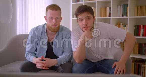两位英俊的白种人成年男子在电视上观看足球比赛并高兴地坐在上面庆祝视频的预览图