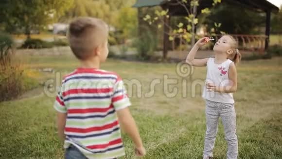 两个有趣的孩子一个男孩和一个女孩在日落时在公园里玩肥皂泡视频的预览图
