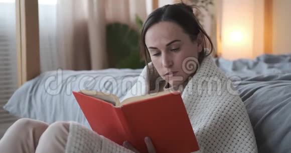女人在家里读一本裹着毯子的书视频的预览图