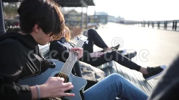 一个年轻人和他的朋友躺在长凳上在户外弹吉他视频的预览图