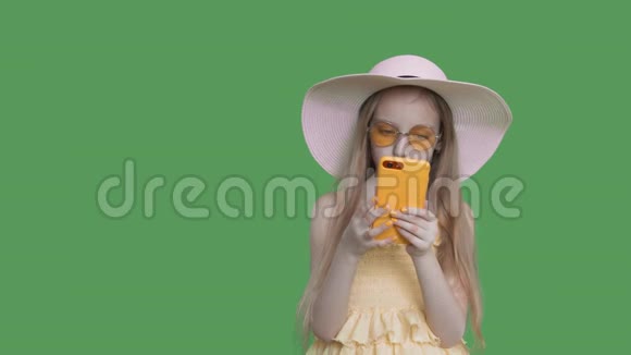 戴夏帽的小女孩在绿色墙背景上读电话阿尔法频道视频的预览图