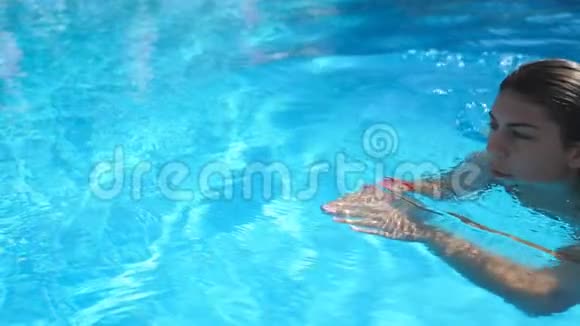 年轻女子清爽在酒店游泳池游泳碧水清澈漂泊在水池边的漂亮姑娘视频的预览图