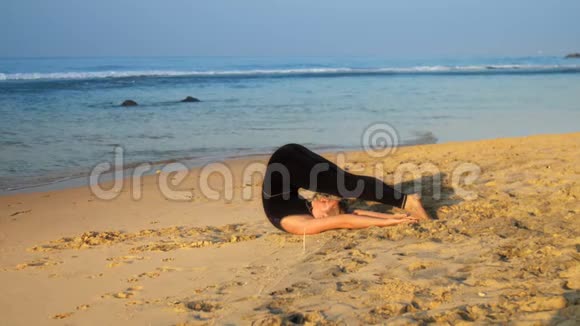 年轻的美女躺在沙滩上做瑜伽姿势视频的预览图