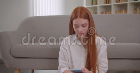 年轻可爱的红头发女性在手机上自拍坐在镜头前摆姿势的特写镜头视频的预览图