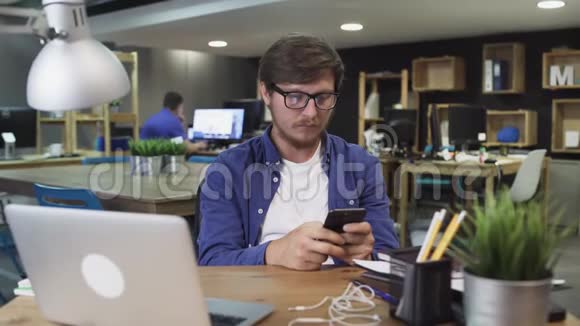 年轻人在办公室里使用智能手机通过互联网手表视频使用社交网络视频的预览图