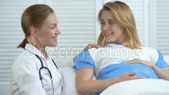 笑容可掬的助产士和孕妇躺在病床上看镜头产前护理视频的预览图