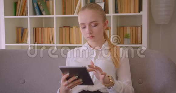 年轻漂亮的白种人金发女学生的特写镜头她用平板电脑看着着视频的预览图