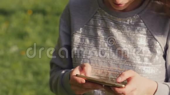 年轻女性在夏天的城市公园散步时在一棵盛开的苹果树的背景下使用智能手机发短信女孩使用视频的预览图