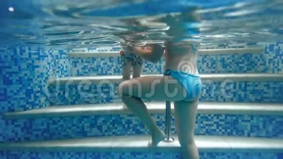 在4K水下视频年轻女子抱着她3岁的蹒跚学步的男孩在游泳池在健身房家庭放松视频的预览图