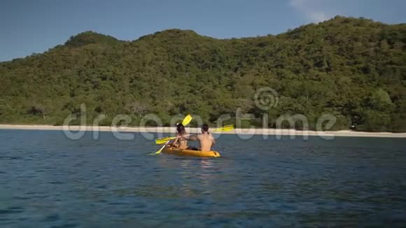 一对朋友在蔚蓝的海洋湾附近的一个野生热带岛屿慢动作皮划艇享受娱乐运动视频的预览图