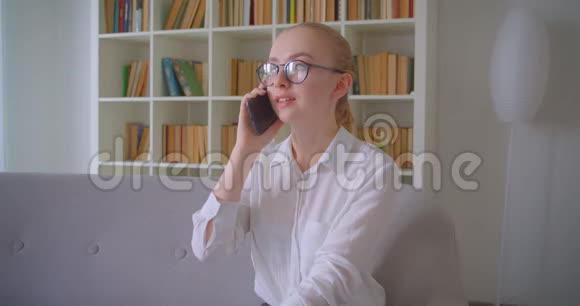 年轻漂亮的白种人金发女学生戴着眼镜打着电话兴高采烈地笑着特写照片视频的预览图