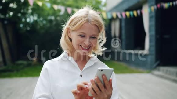 快乐的女人用智能手机看屏幕微笑站在户外视频的预览图