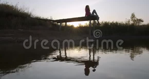 美丽的女孩凝视着坐在码头上的湖视频的预览图