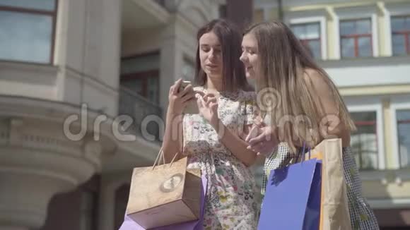 两个可爱的女朋友购物后带着购物袋在户外手机上自拍快乐女孩的休闲视频的预览图