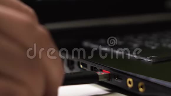 关闭男性手连接一个黑色USB电缆到笔记本电脑与发光红色USB端口视频的预览图