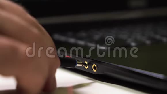 男性手将音频电缆连接到现代黑色笔记本电脑上耳机和麦克风断开音频电缆视频的预览图
