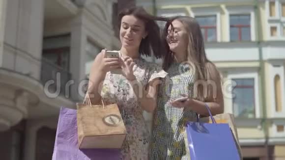 两个幸福的女朋友在美丽的建筑前用手机发短信购物后视频的预览图